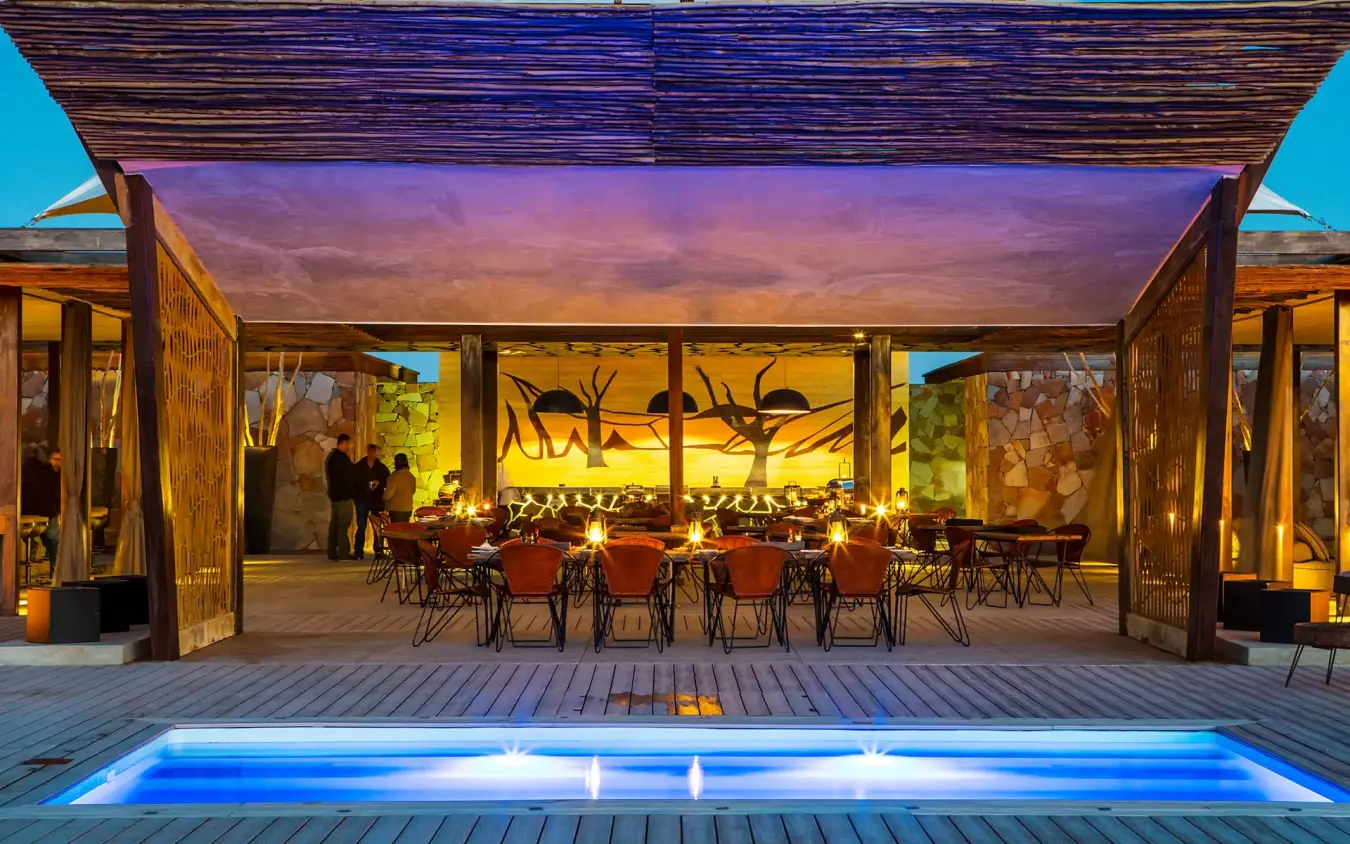 Evening dining pavilion with illuminated wildlife artwork and pool, Dead Valley Lodge, Sossusvlei, Namibia