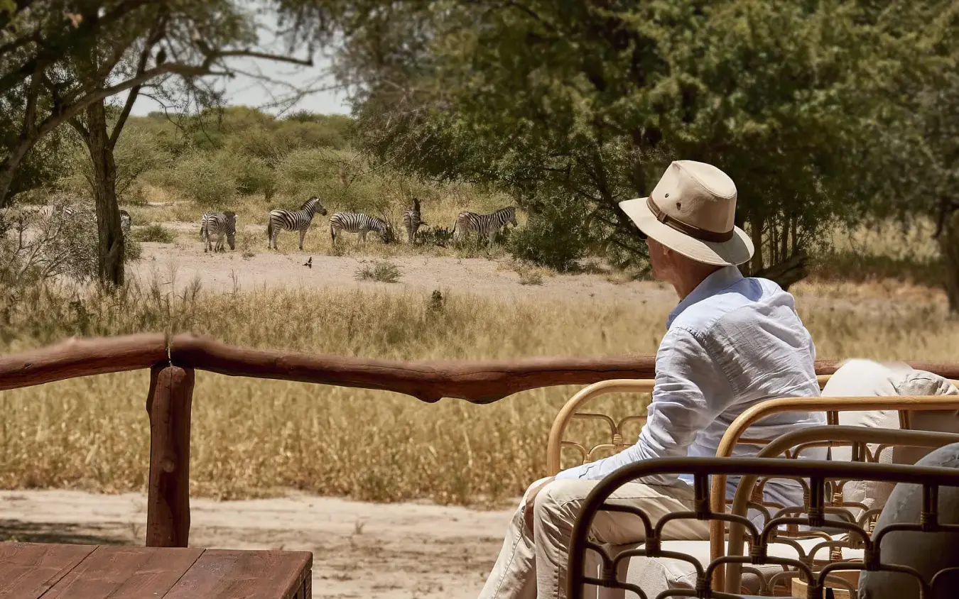Guest observing wildlife from lodge deck at sunset, Deception Valley Lodge, Central Kalahari, Botswana