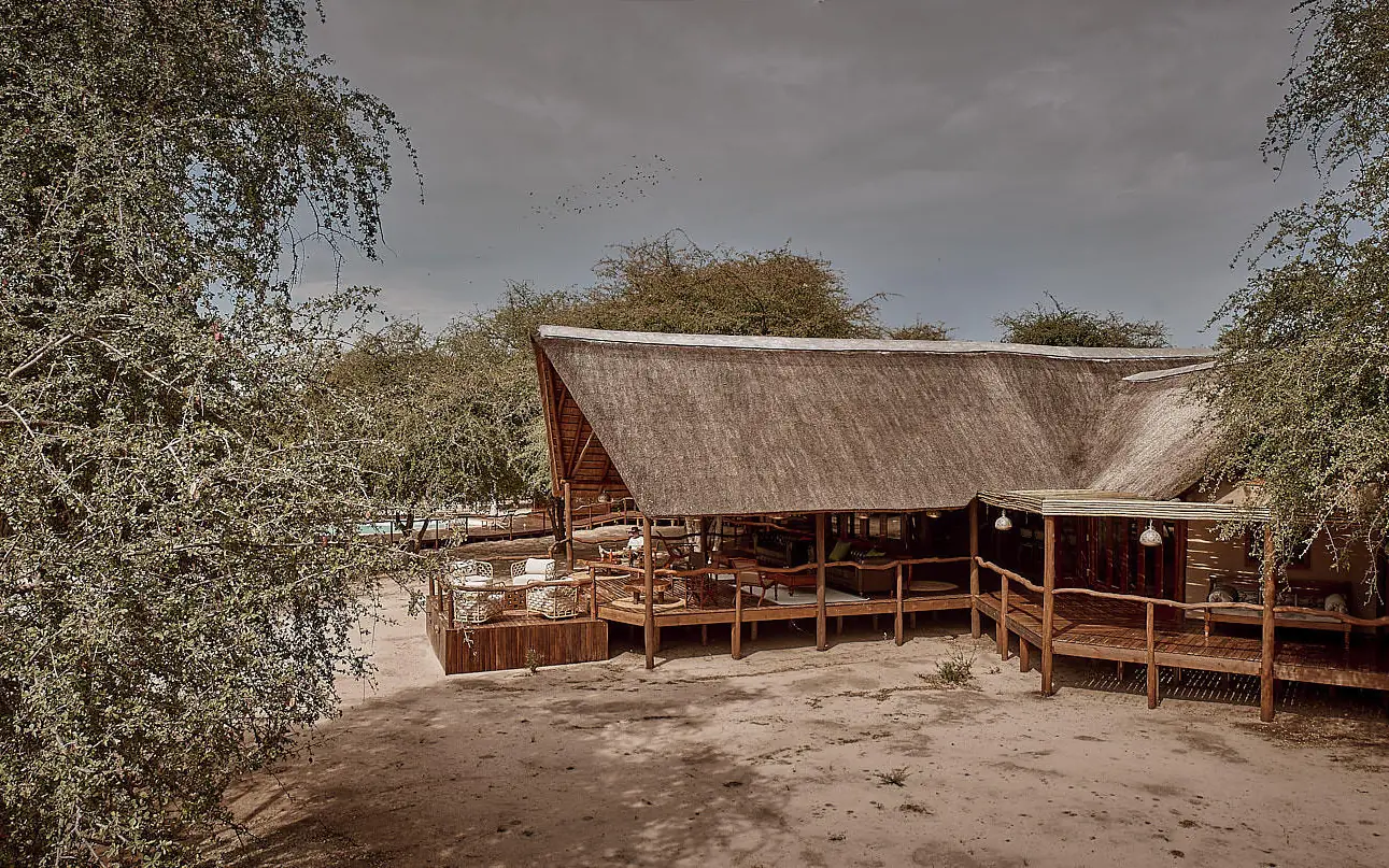 Thatched-roof lodge building with wooden deck and surrounding trees, Deception Valley Lodge, Central Kalahari, Botswana
