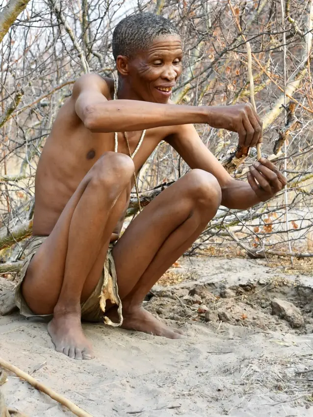 Young person crouching by fallen log in woodland, Deception Valley Lodge, Central Kalahari, Botswana