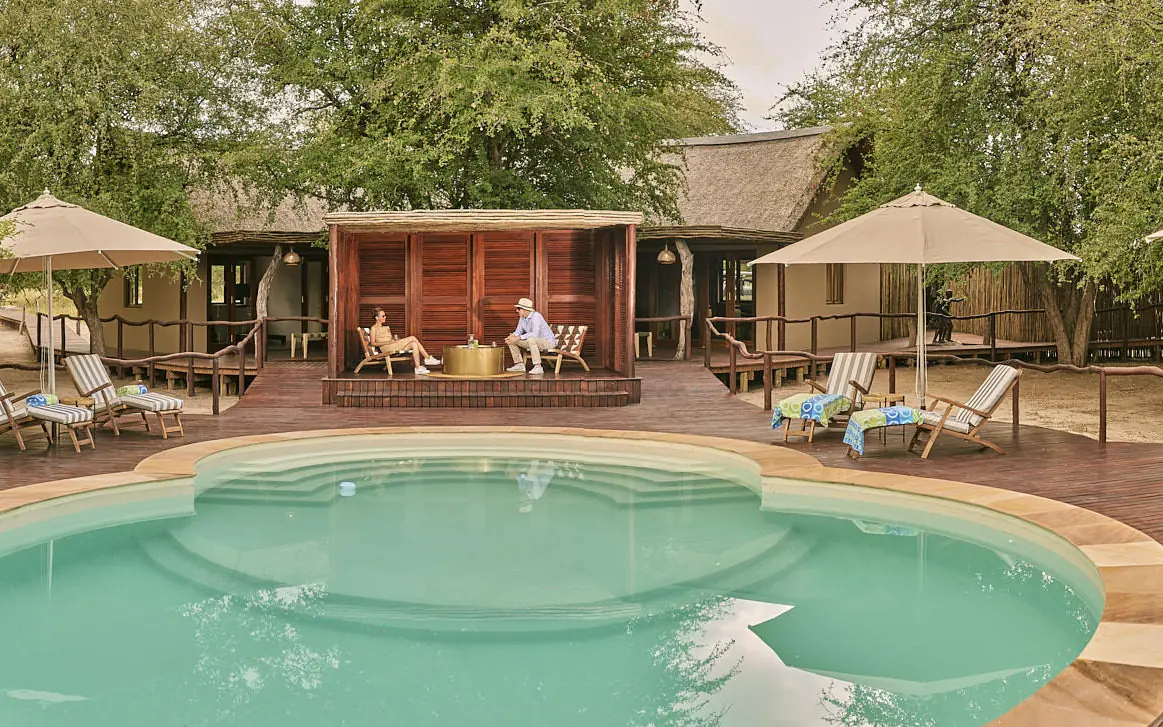 Resort pool with lounge chairs and thatched umbrellas surrounding, Deception Valley Lodge, Central Kalahari, Botswana