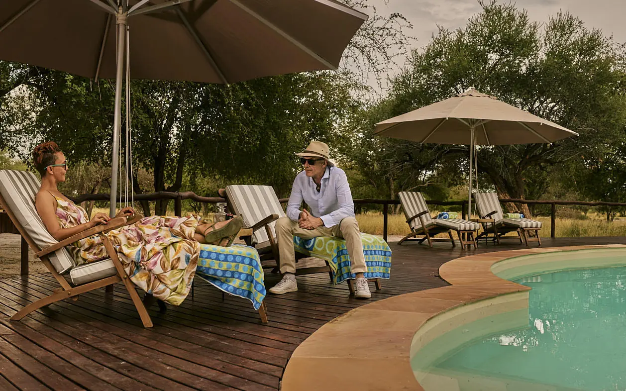Guests relaxing by resort pool deck under umbrellas, Deception Valley Lodge, Central Kalahari, Botswana