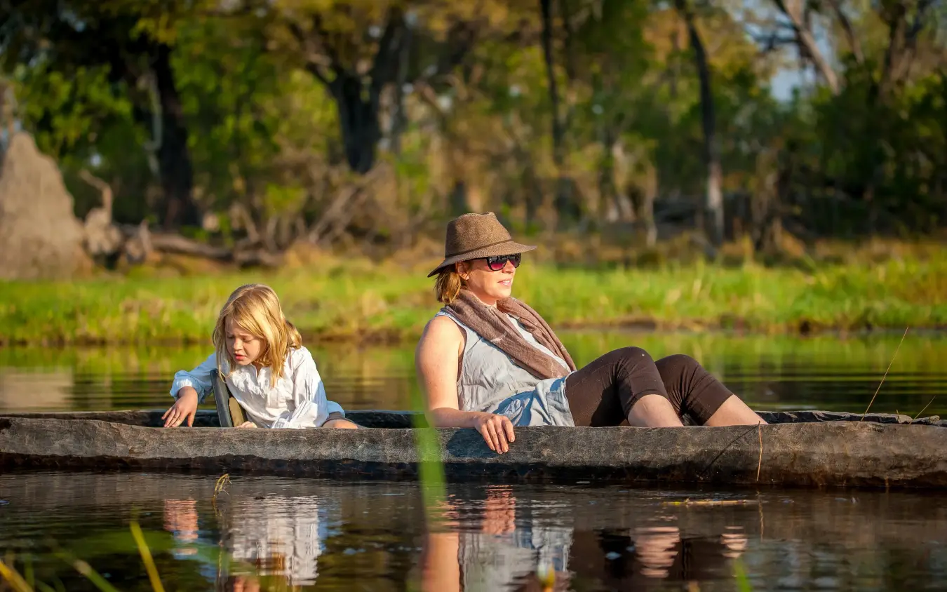 Adult and child in traditional dugout canoe on waterway, Delta Camp, The Okavango Delta, Botswana