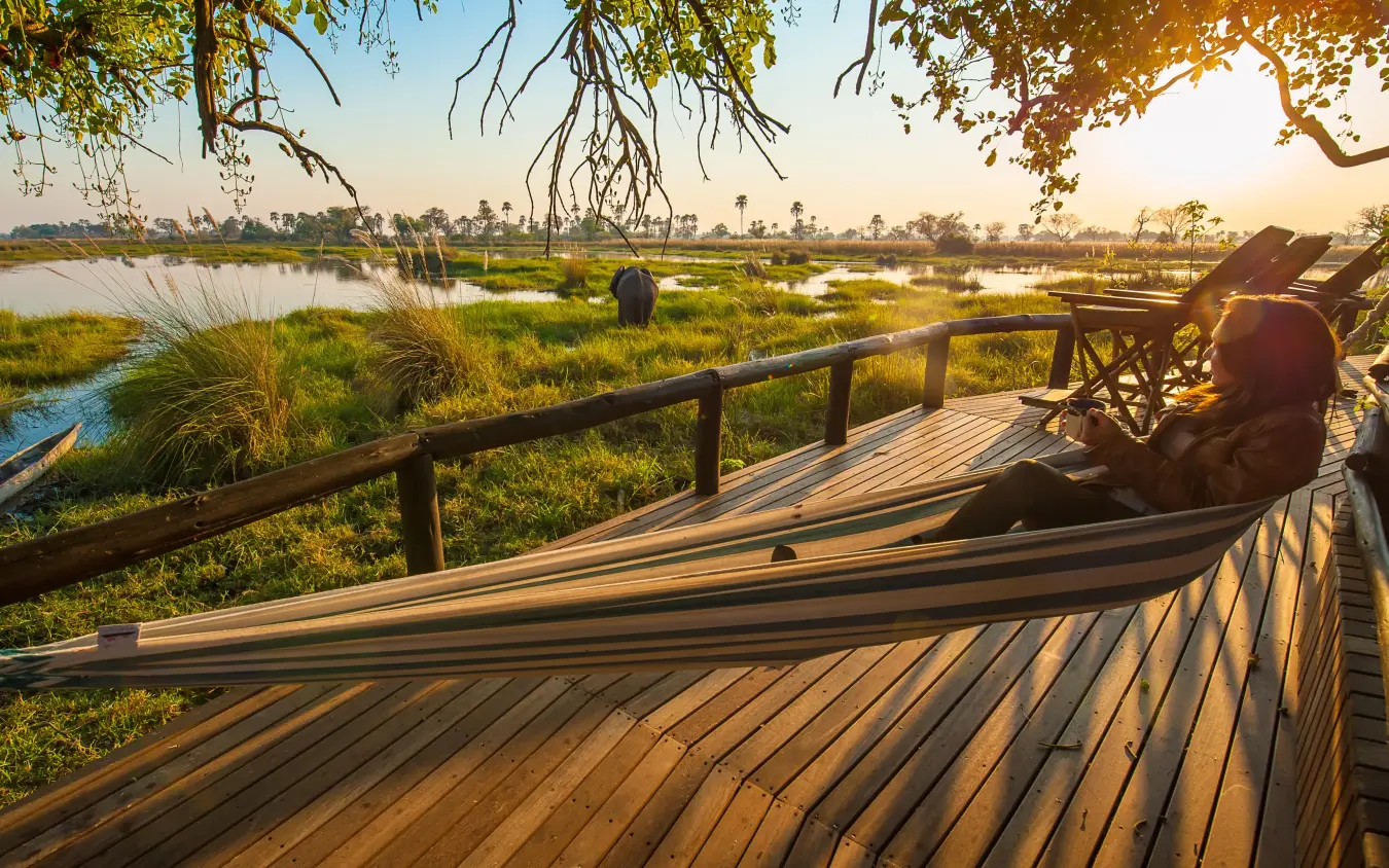 Person relaxing on wooden deck overlooking wetland landscape, Delta Camp, The Okavango Delta, Botswana