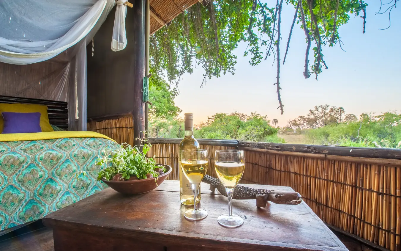 Wooden deck with wine glasses overlooking delta landscape, Delta Camp, The Okavango Delta, Botswana