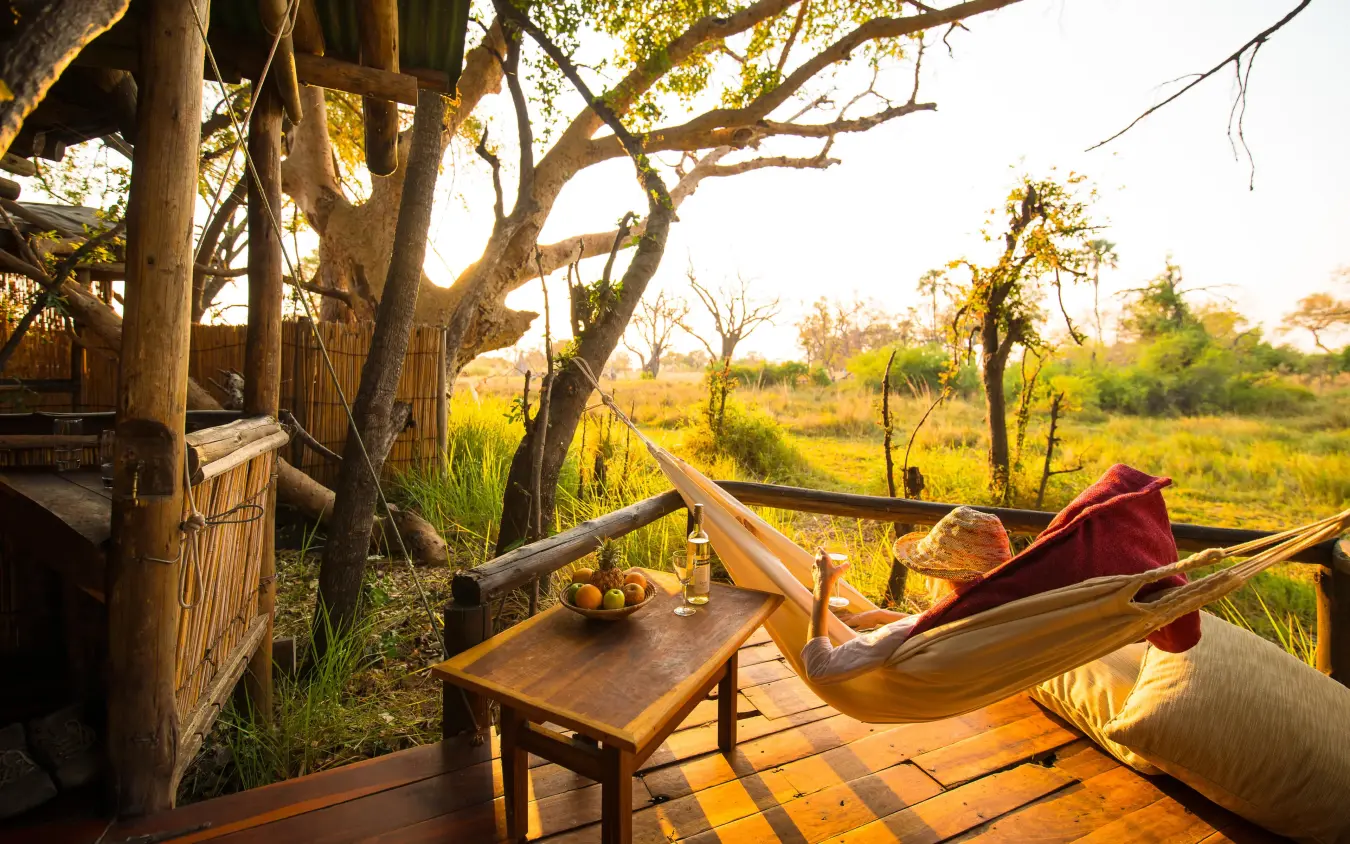 Person relaxing in hammock on wooden deck overlooking savanna, Delta Camp, The Okavango Delta, Botswana