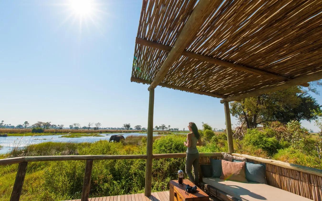Woman standing on wooden deck overlooking wetland landscape, Delta Camp, The Okavango Delta, Botswana