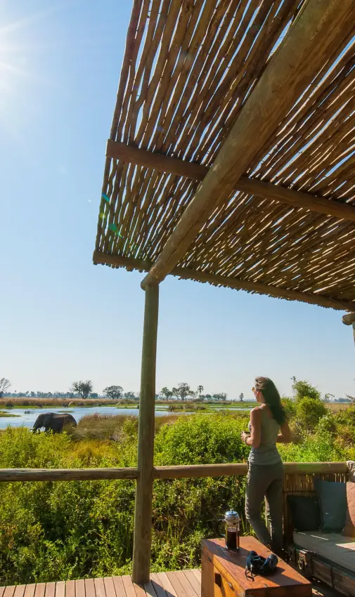 Woman standing on wooden deck overlooking wetland landscape, Delta Camp, The Okavango Delta, Botswana