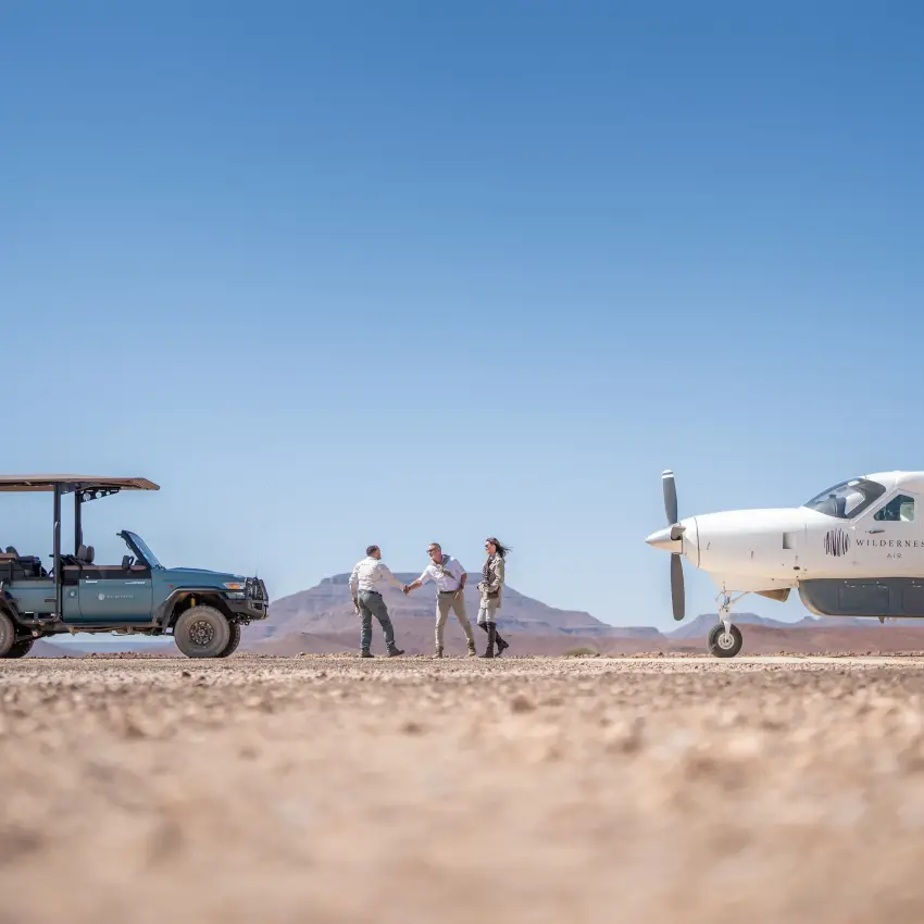Safari vehicle and guests meeting light aircraft on desert airstrip, Desert Rhino Camp, Damaraland, Namibia