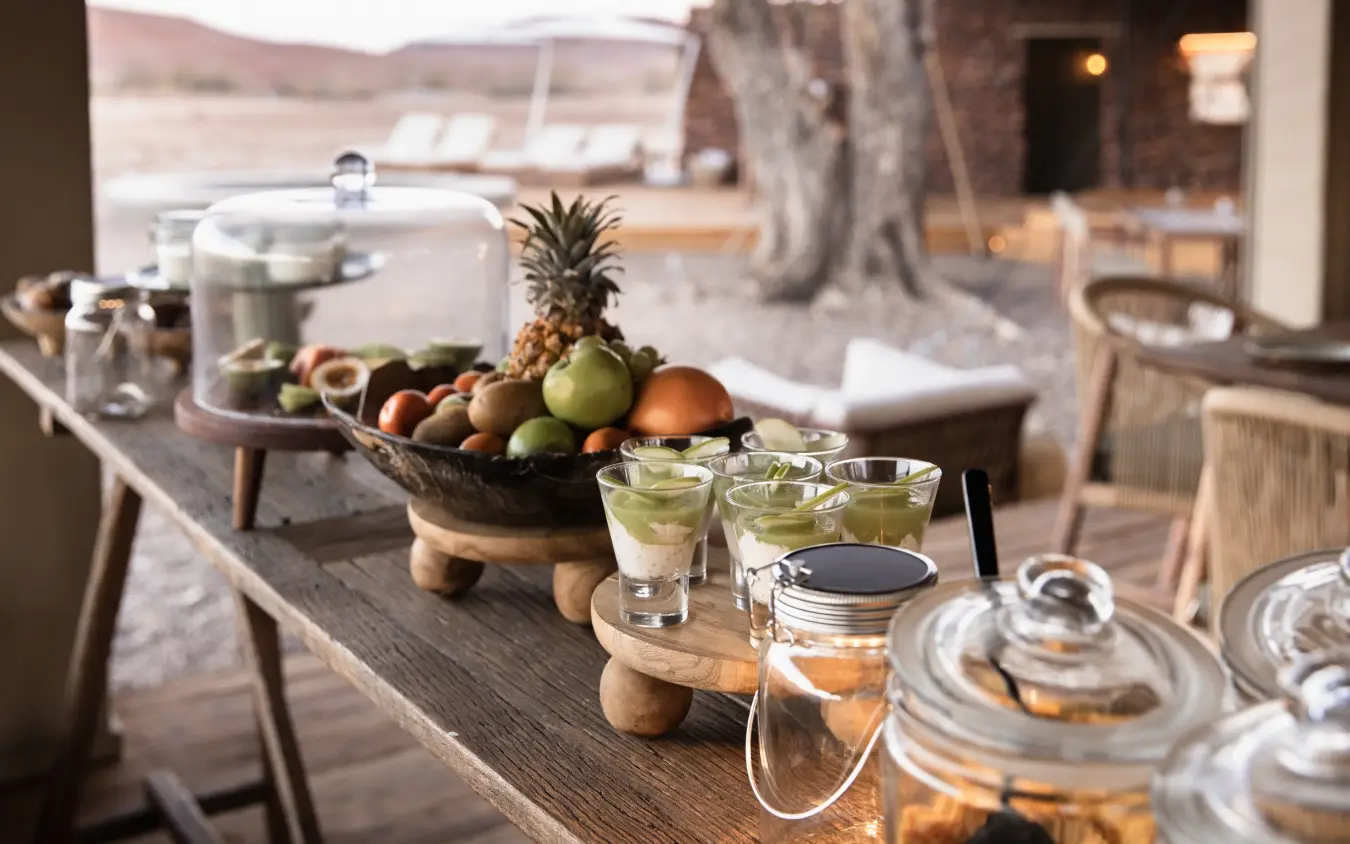 Outdoor dining table with fruit bowl and glassware overlooking savanna landscape, Desert Rhino Camp, Damaraland, Namibia
