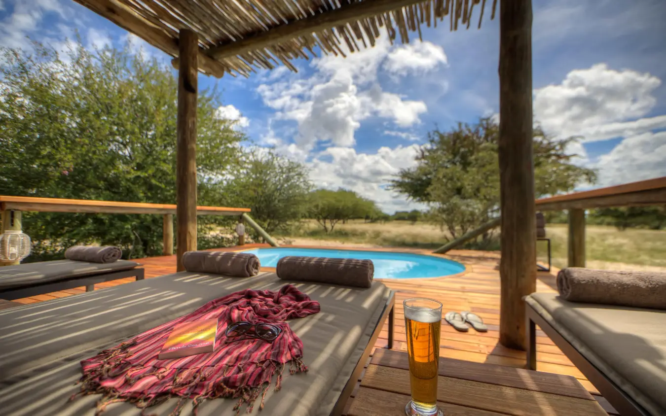 Wooden deck with loungers overlooking blue pool and savanna, Dinaka, Central Kalahari, Botswana