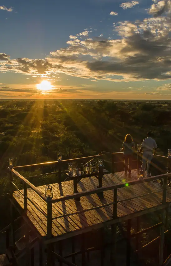 Couple watching sunset from elevated wooden deck platform, Dinaka, Central Kalahari, Botswana