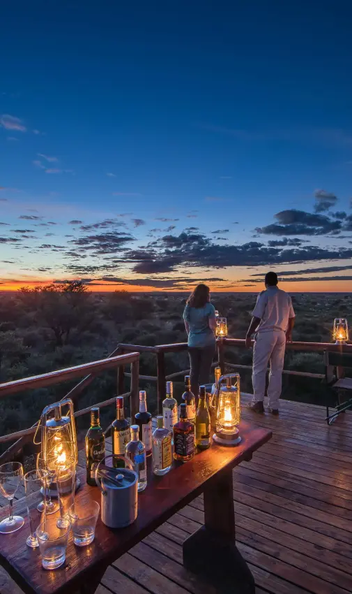 Couple enjoying sunset from wooden deck overlooking savanna, Dinaka, Central Kalahari, Botswana