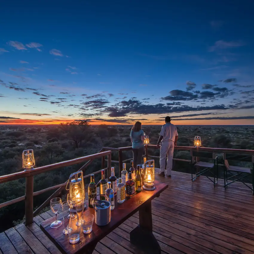 Couple enjoying sunset from wooden deck overlooking savanna, Central Kalahari, Botswana