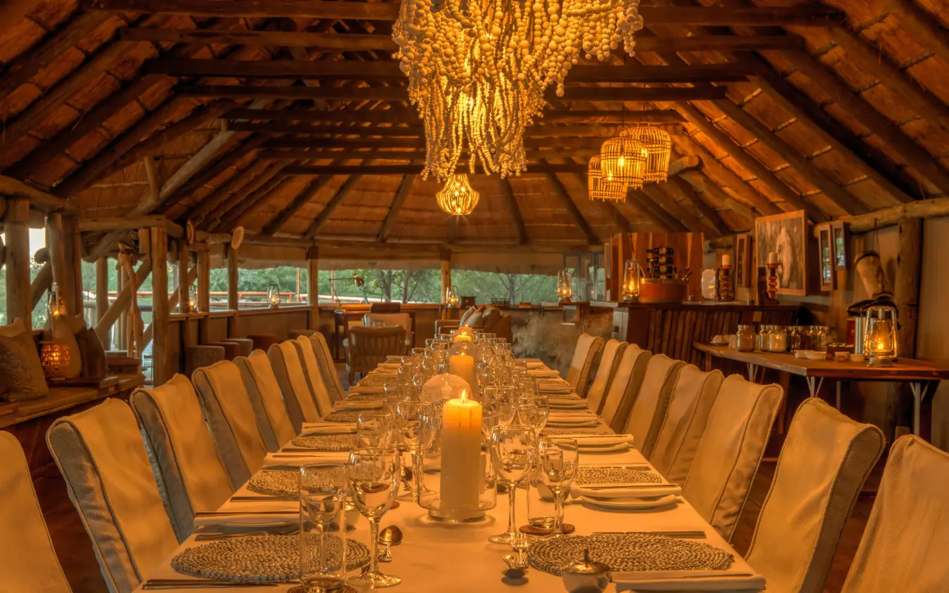 Long dining table set for evening service under wooden beams, Dinaka, Central Kalahari, Botswana