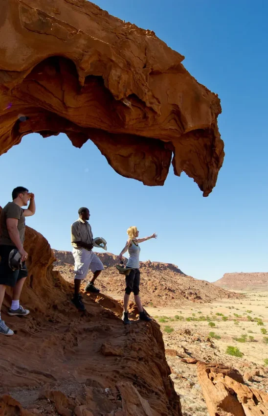 Hikers exploring natural rock arch formation in arid desert landscape, Doro Nawas Camp, Damaraland, Namibia