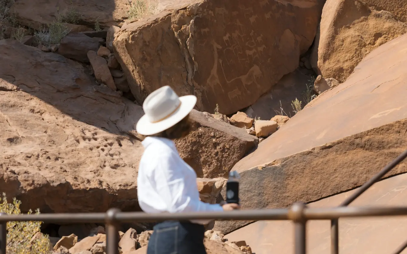 Tourist photographing ancient petroglyphs on desert rock formation, Doro Nawas Camp, Damaraland, Namibia
