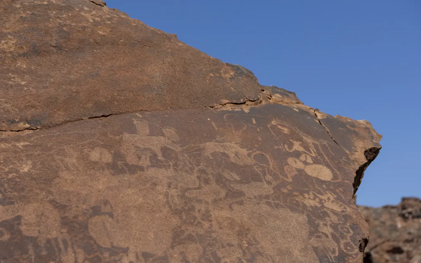 Ancient rock petroglyphs on desert boulder under clear blue sky, Doro Nawas Camp, Damaraland, Namibia