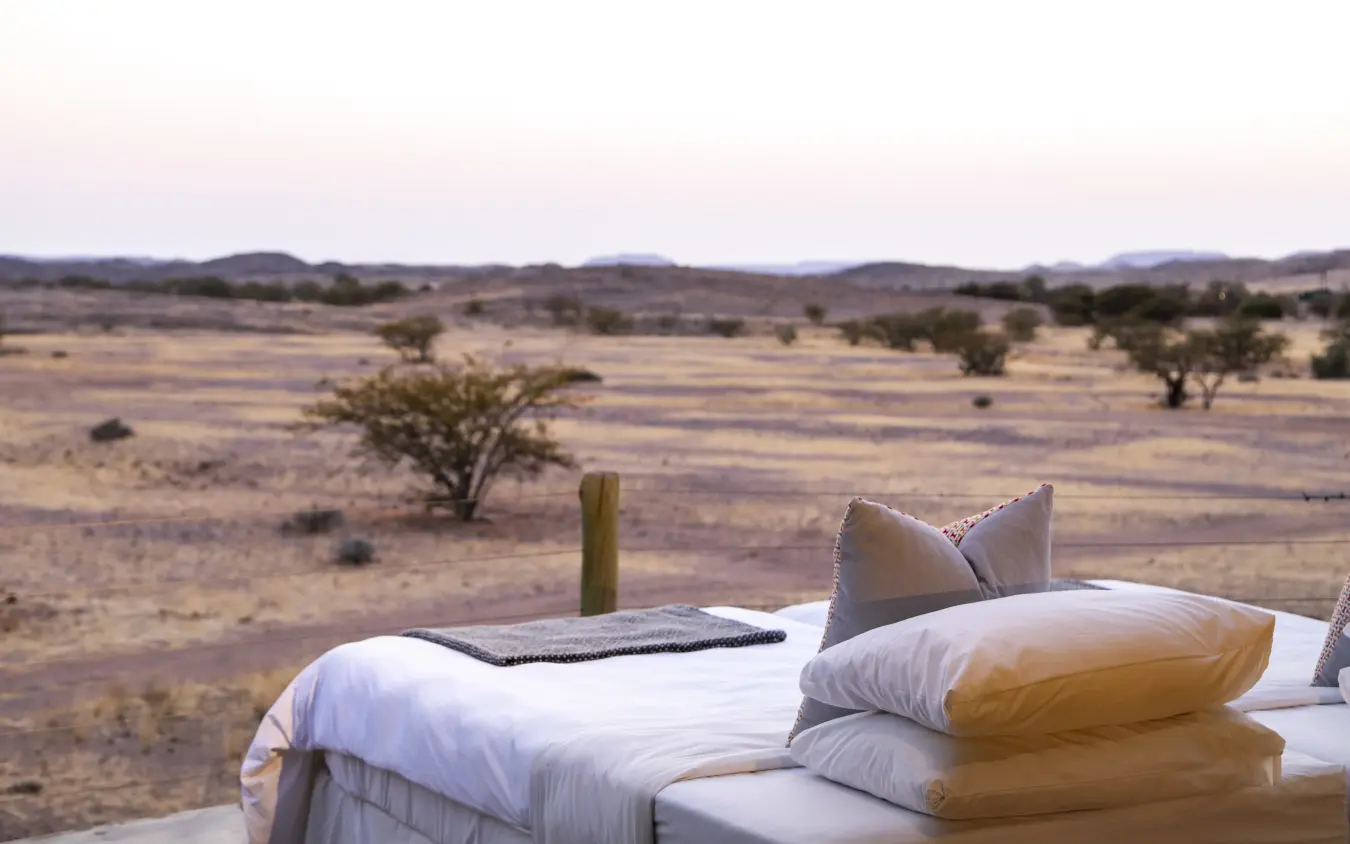 Bed with white linens overlooking arid savanna landscape at dusk, Doro Nawas Camp, Damaraland, Namibia