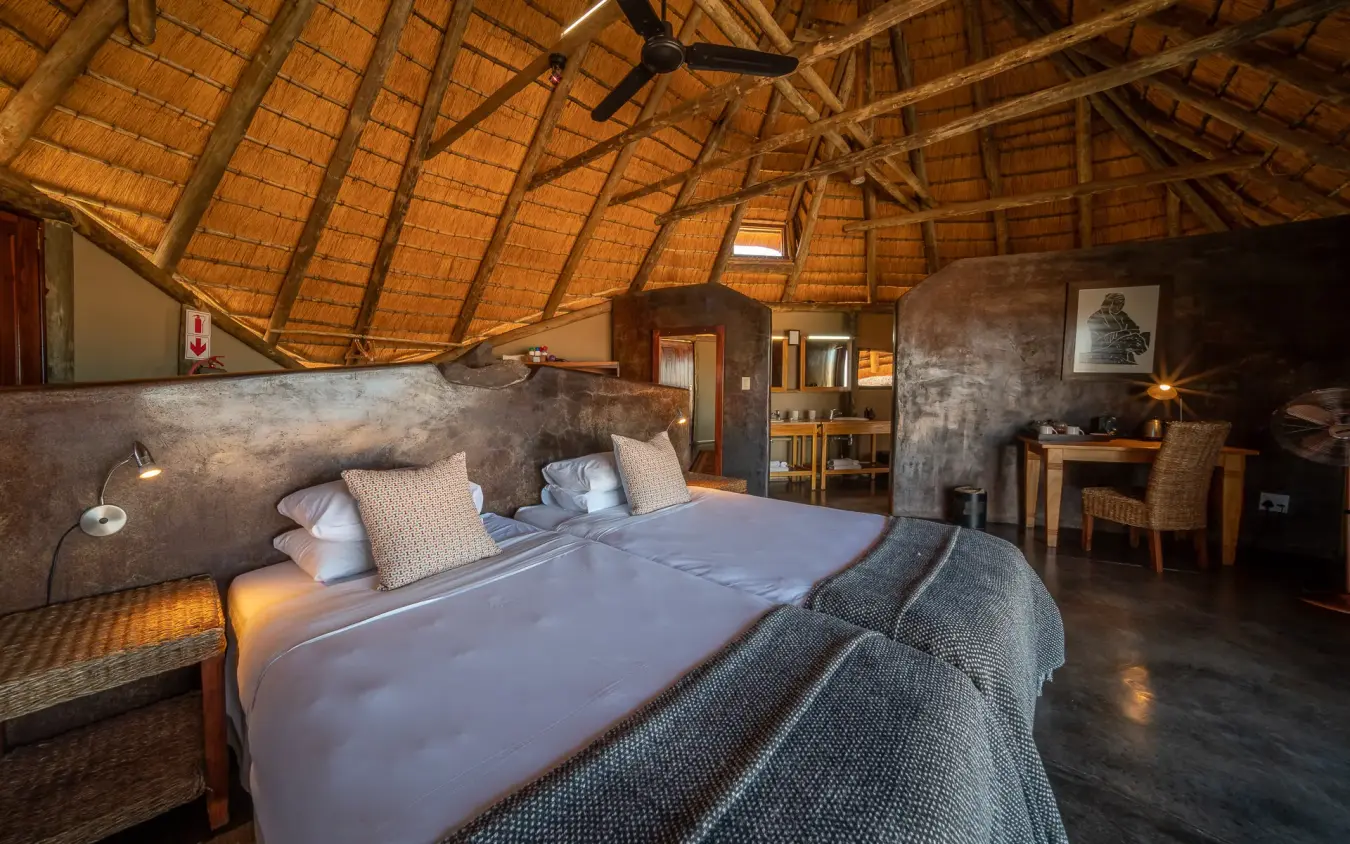 Luxury safari lodge bedroom with thatch roof and concrete walls at dusk, Doro Nawas Camp, Damaraland, Namibia