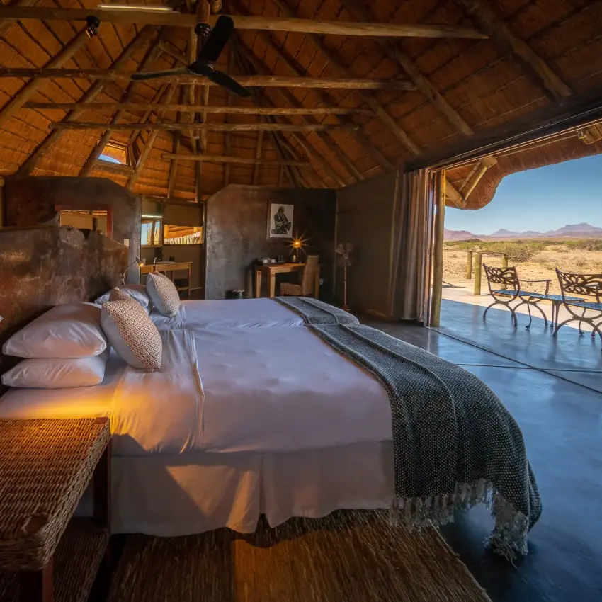 Luxury safari bedroom with open-air terrace overlooking arid landscape at dusk, Doro Nawas Camp, Damaraland, Namibia