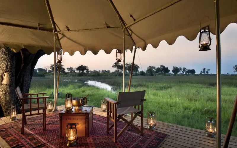 Canvas tent lounge overlooks wetland with waterway at dusk, Duba Explorers Camp, The Okavango Delta, Botswana