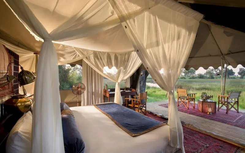 Luxury safari tent bedroom with sheer canopy and savanna views, Duba Explorers Camp, The Okavango Delta, Botswana