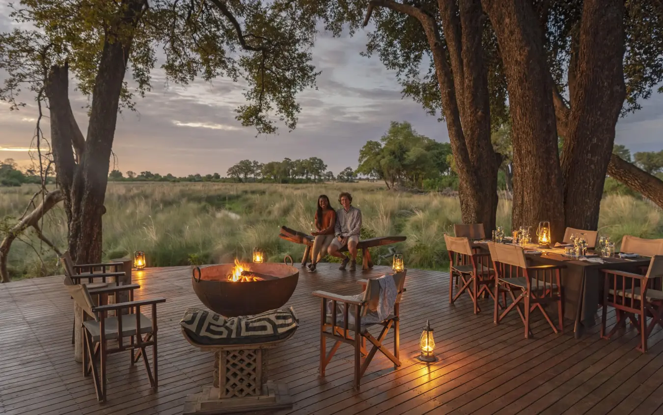 Wooden deck beneath ancient trees with fire pit and savanna, Duba Explorers Camp, The Okavango Delta, Botswana