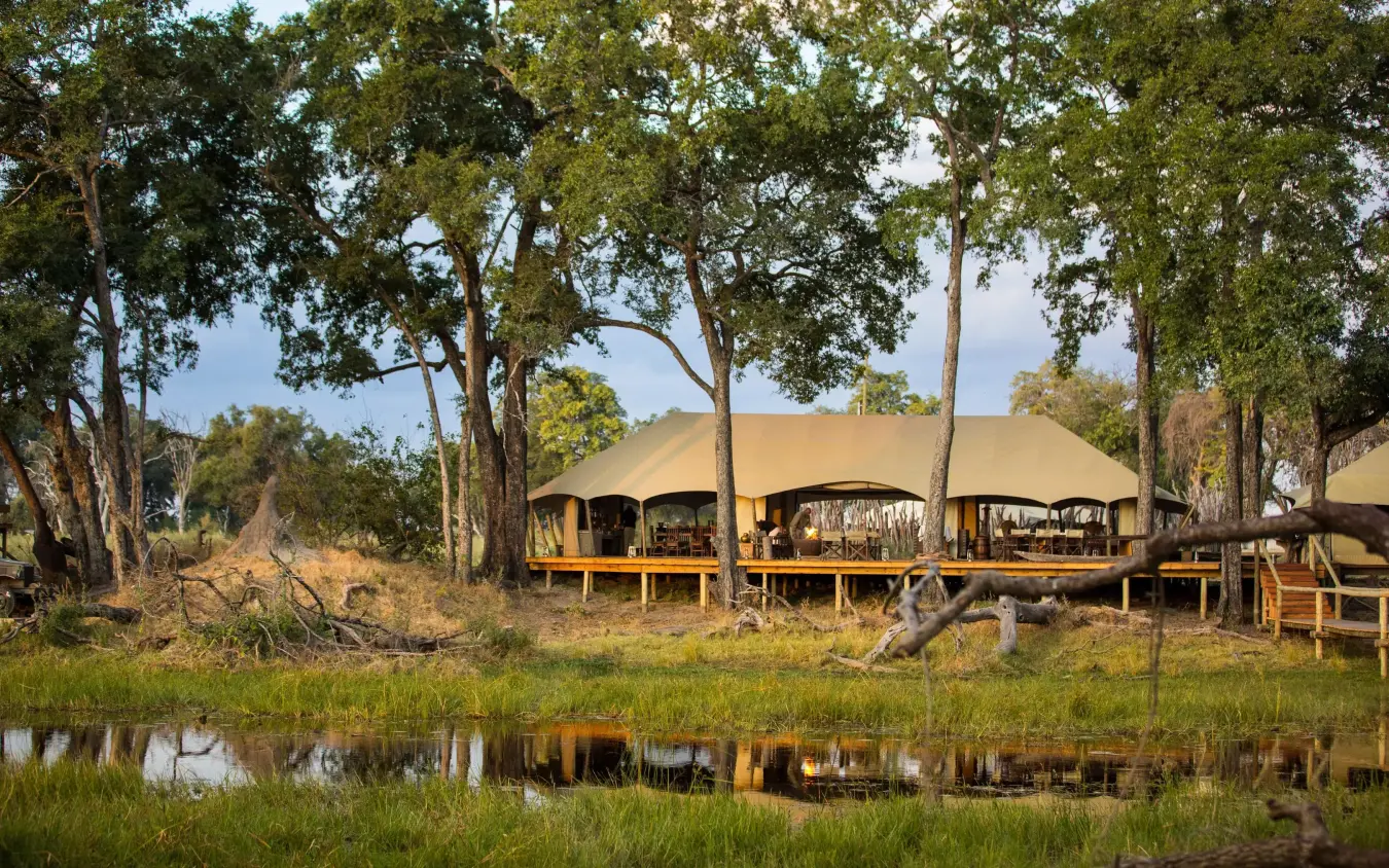 Canvas safari tents reflected in waterhole at dusk, Duba Explorers Camp, The Okavango Delta, Botswana