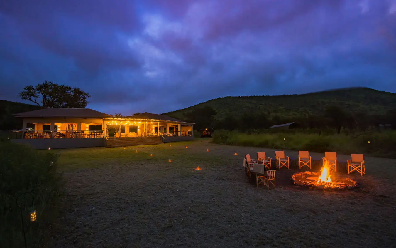 Safari lodge at dusk with campfire and seating area, Dunia Camp, Serengeti National Park, Tanzania