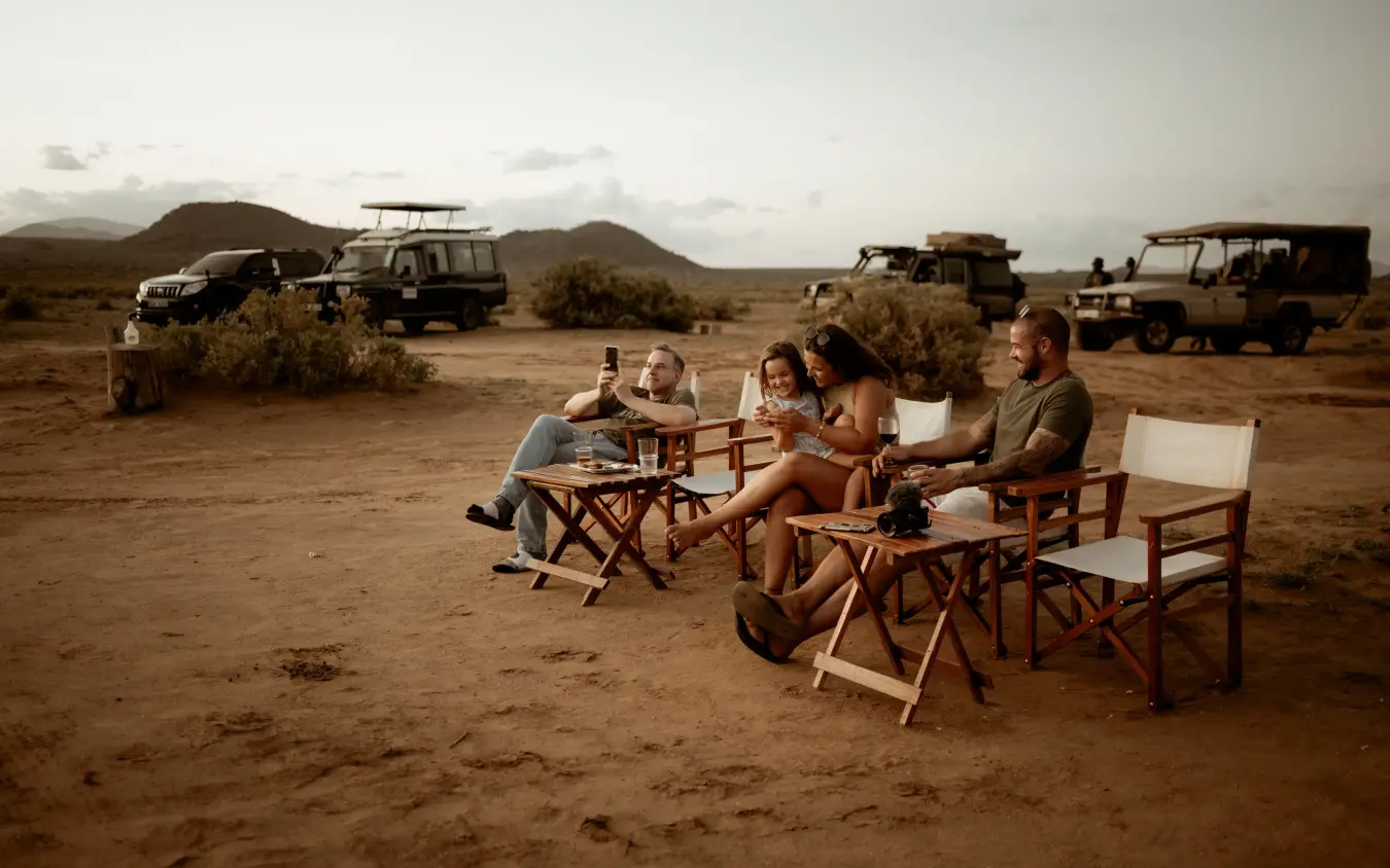 Group of safari guests gathered around campfire in desert landscape at dusk, Elephant Bedroom Camp, Samburu Reserve, Kenya