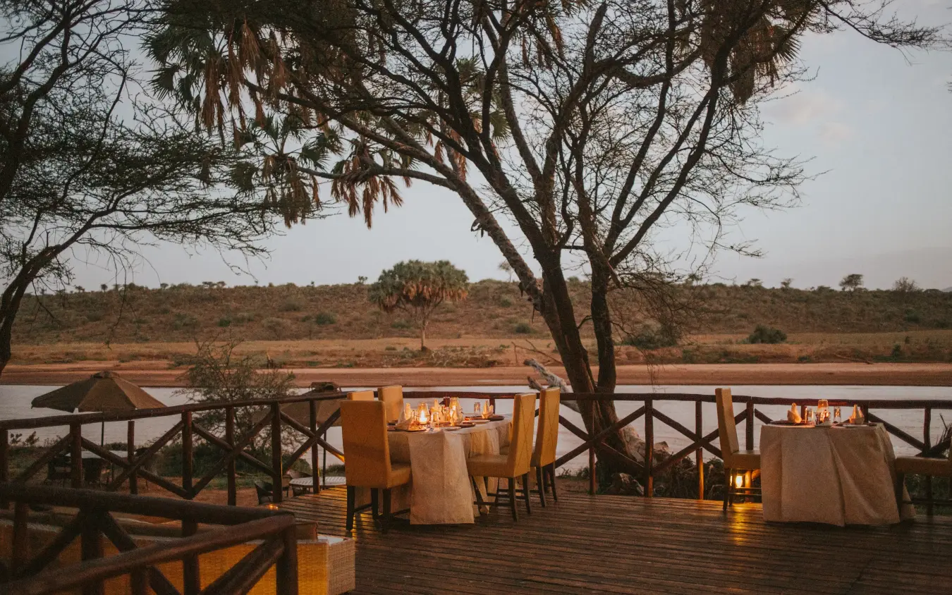 Dining tables set on wooden deck overlooking river at dusk, Elephant Bedroom Camp, Samburu Reserve, Kenya