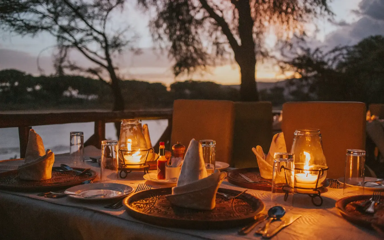 Candlelit dinner table overlooking waterside at dusk with lanterns, Elephant Bedroom Camp, Samburu Reserve, Kenya