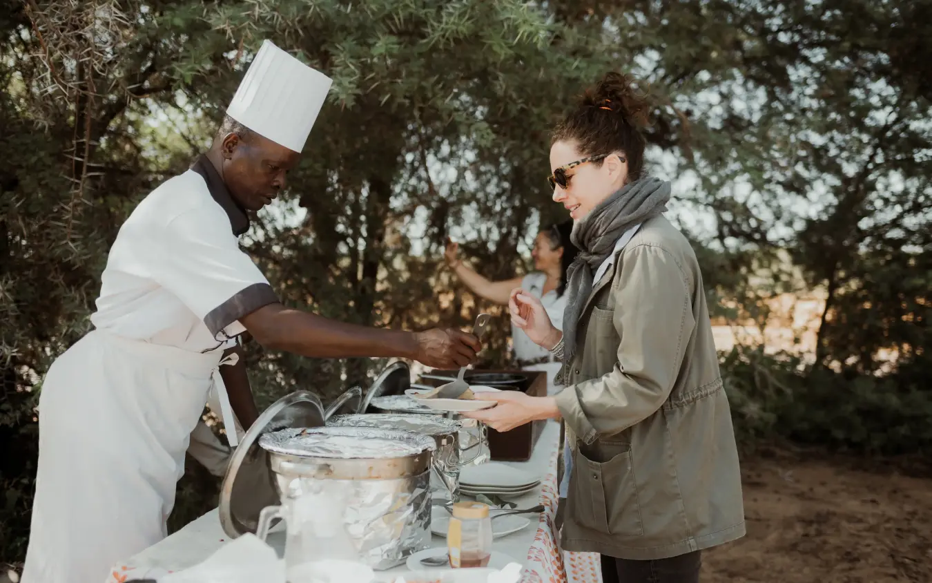 Chef serving food to guest at outdoor dining setup under trees, Elephant Bedroom Camp, Samburu Reserve, Kenya