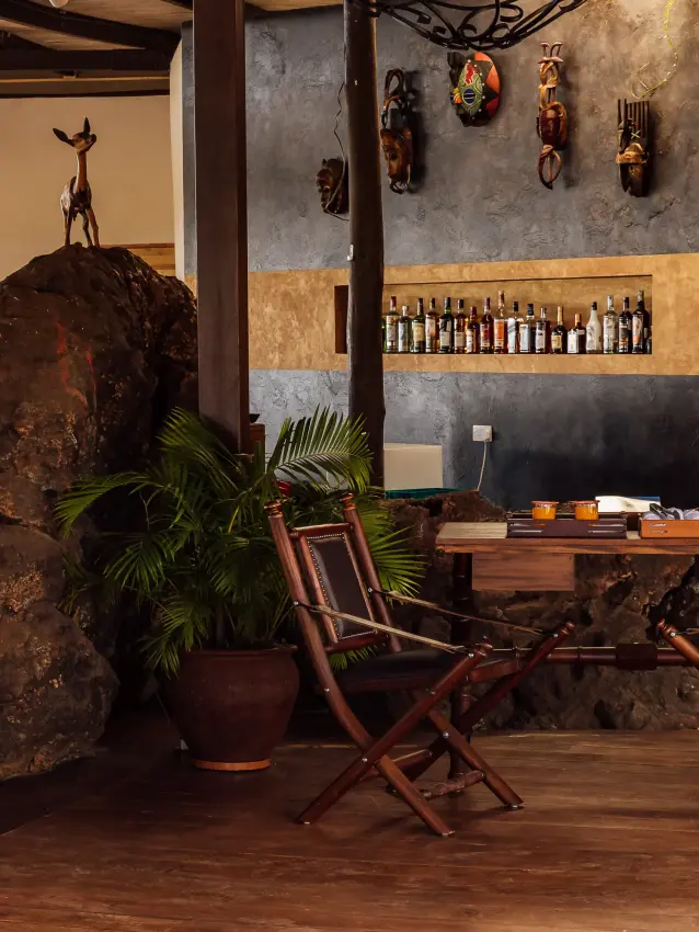 Large boulder beside wooden table and chairs in rustic lodge interior, Elephant Gorge Camp, Amboseli and Chyulu Hills, Kenya