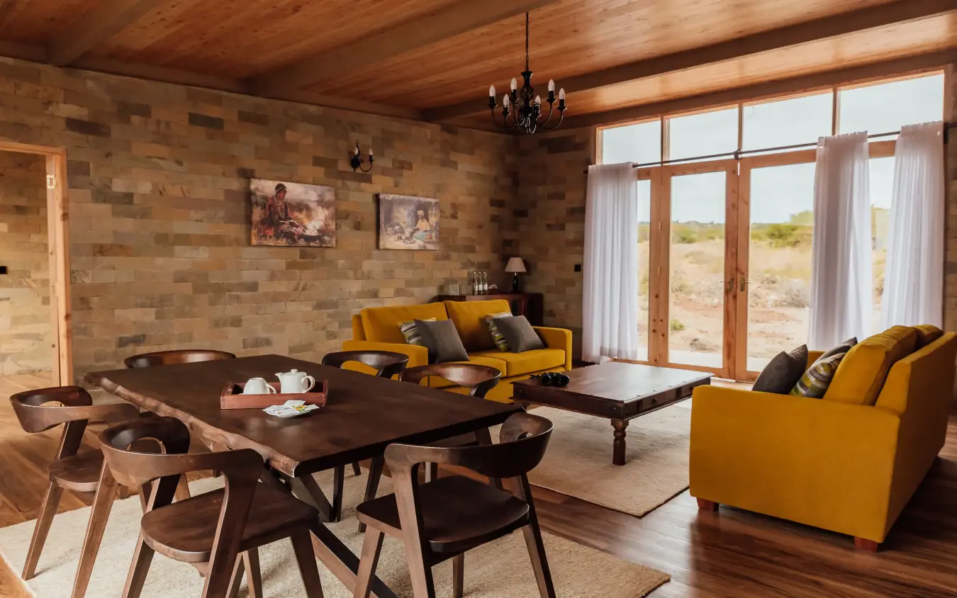 Modern lodge interior with mustard sofas and dining area overlooking arid landscape, Elephant Gorge Camp, Amboseli and Chyulu Hills, Kenya