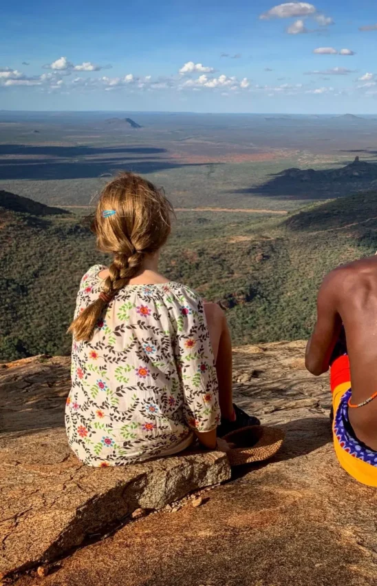 Two children sitting on rock overlooking vast landscape, Elephant Watch Camp, Samburu Reserve, Kenya