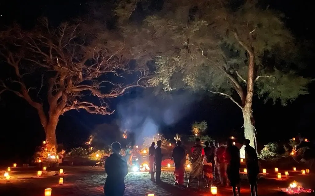 Guests gather around candlelit evening event under trees, Elephant Watch Camp, Samburu Reserve, Kenya