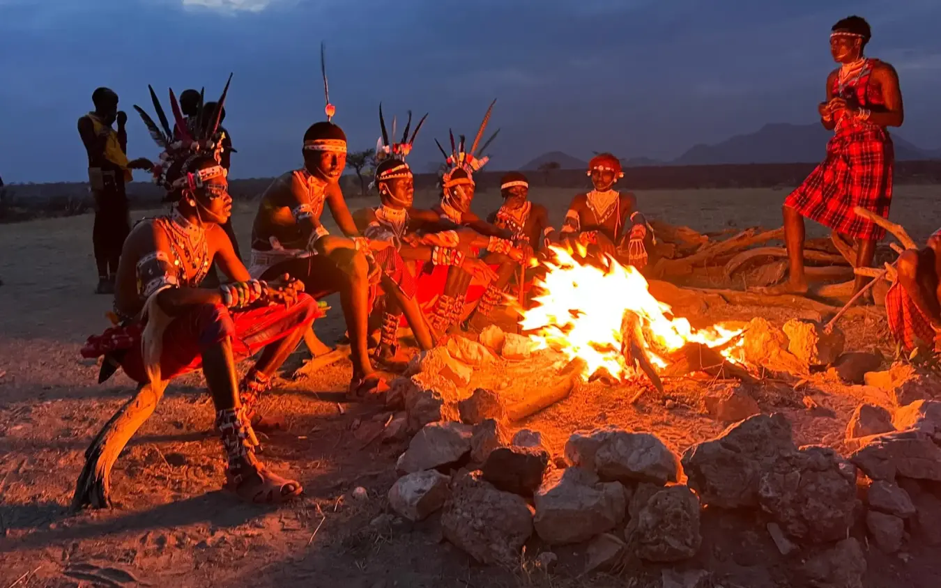 Indigenous people gathered around evening campfire at dusk, Elephant Watch Camp, Samburu Reserve, Kenya