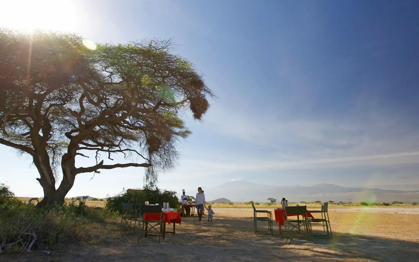 Outdoor dining setup beneath acacia tree in savanna, Tortilis Camp, Amboseli and Chyulu Hills, Kenya
