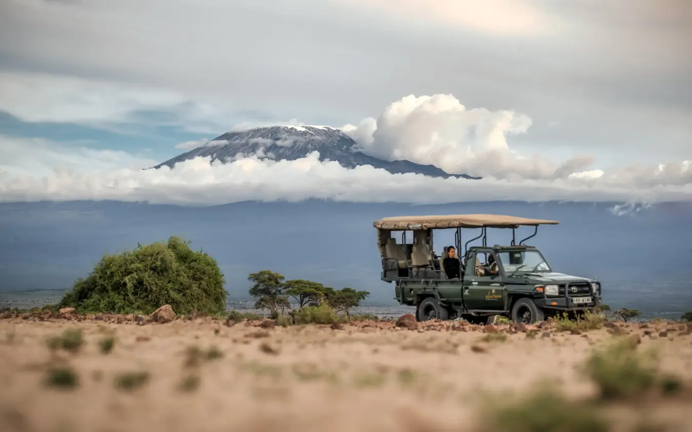 Safari vehicle on dusty plains with snow-capped mountain backdrop, Tortilis Camp, Amboseli and Chyulu Hills, Kenya