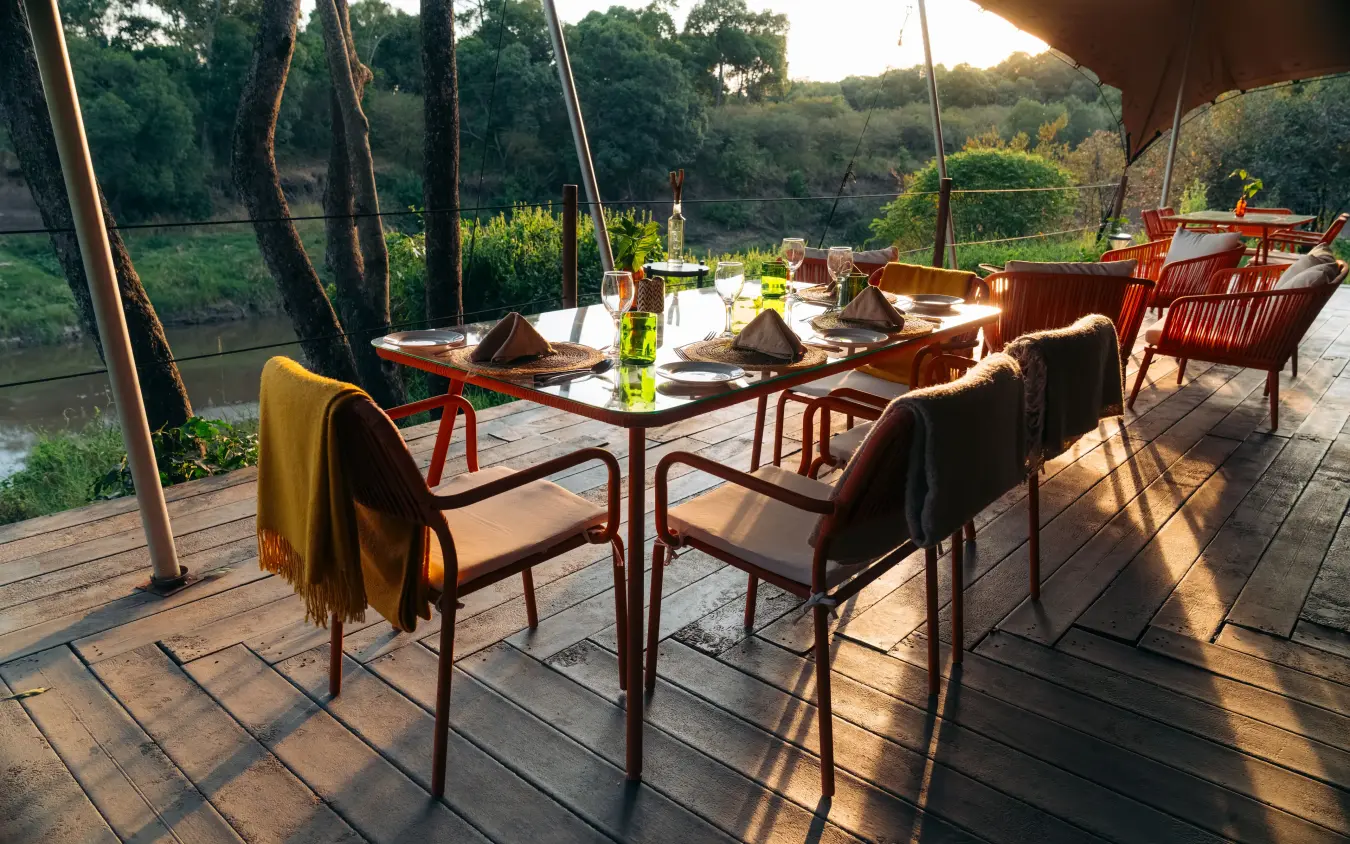 Riverside dining deck with table settings at sunset, Emboo Camp, Maasai Mara, Kenya