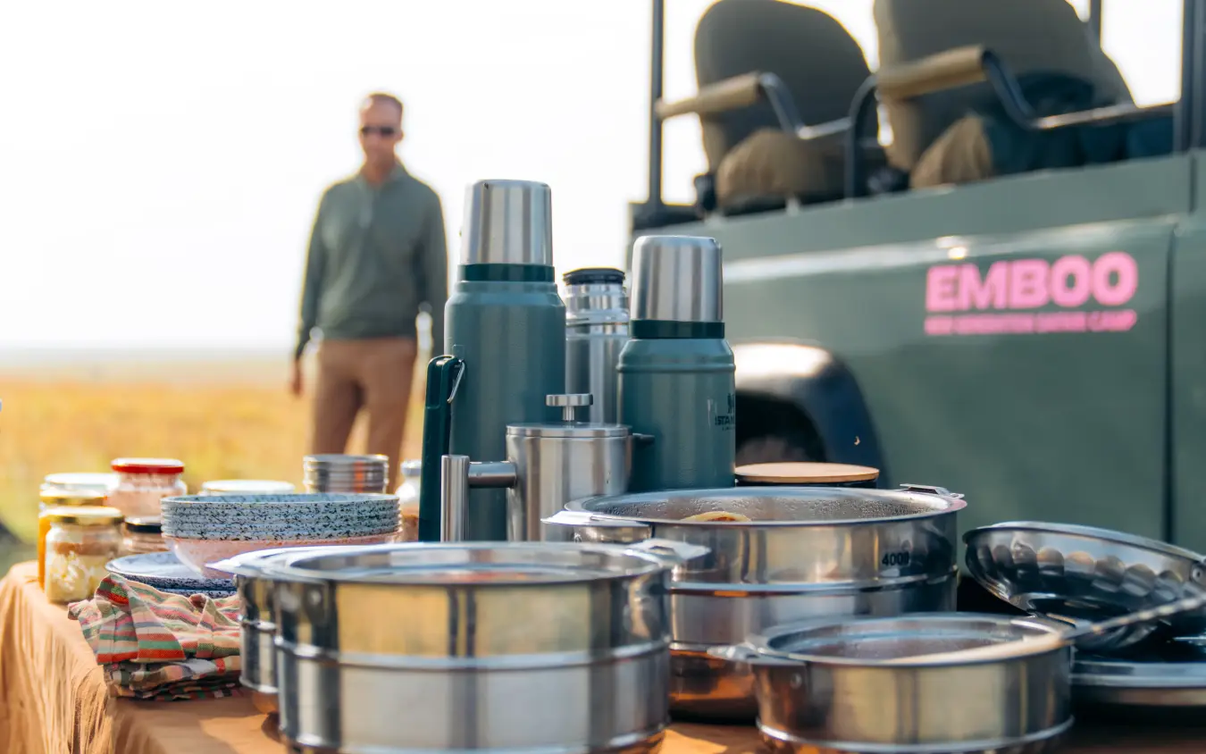 Camp dining setup with cookware and safari vehicle backdrop, Emboo Camp, Maasai Mara, Kenya