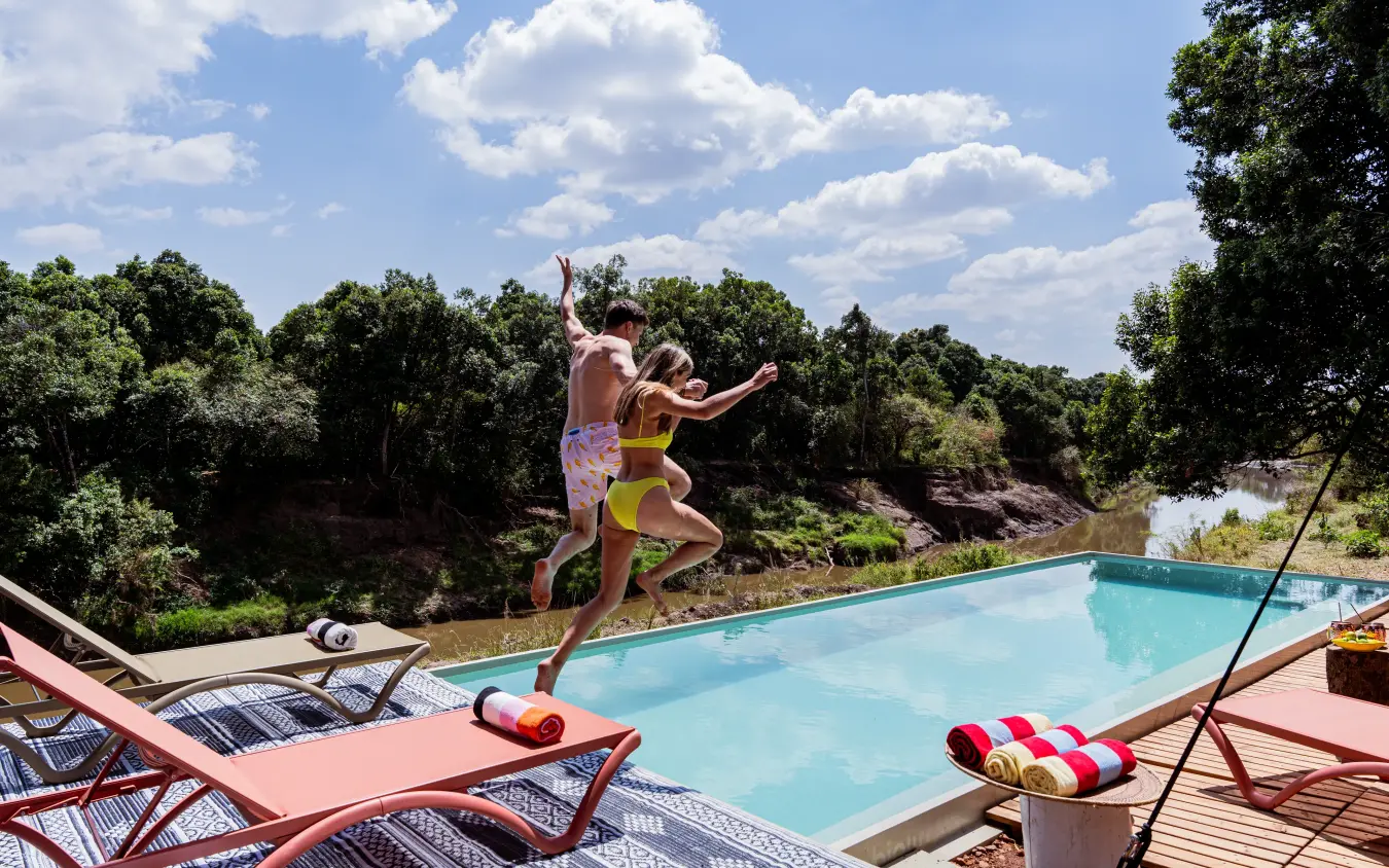 Children jumping into turquoise pool overlooking riverine landscape, Emboo Camp, Maasai Mara, Kenya