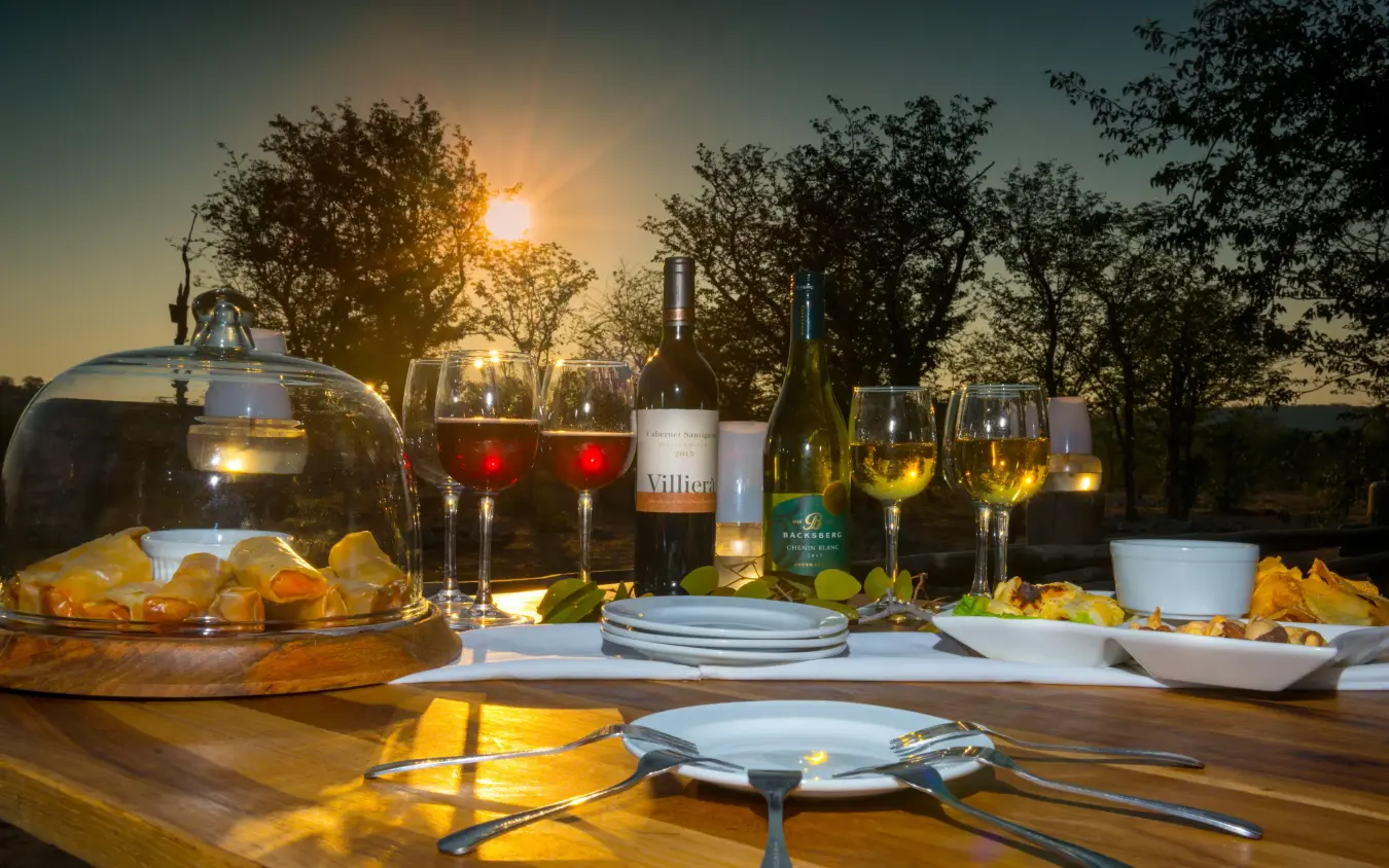 Outdoor dinner table set with wine and snacks at sunset, Encounter by Ongava, Etosha National Park, Namibia