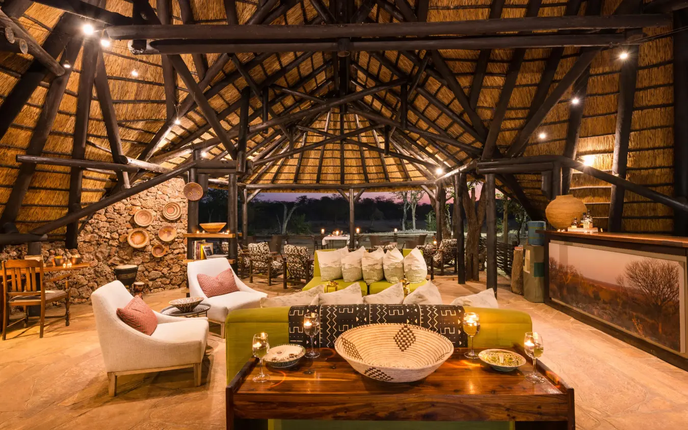 Thatched lodge interior with seating and dining setup at night, Encounter by Ongava, Etosha National Park, Namibia