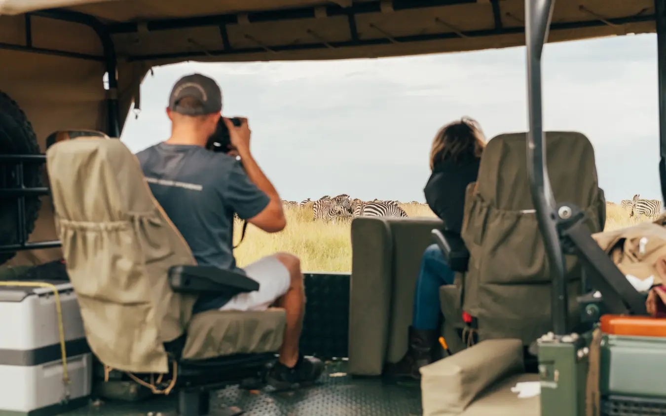 Guests photographing zebras from open safari vehicle, Encounter Mara Camp, Maasai Mara, Kenya