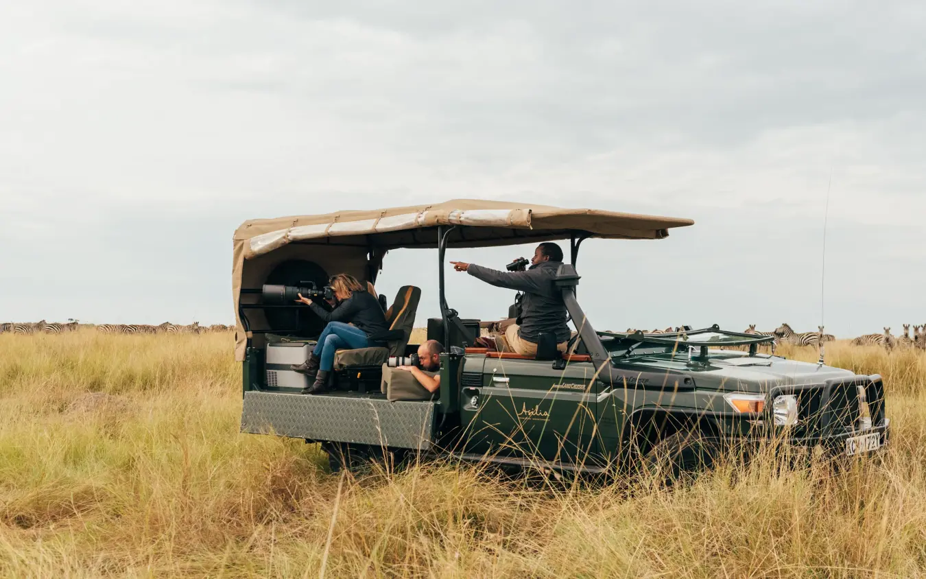 Safari vehicle with guests on game drive in grassland, Encounter Mara Camp, Maasai Mara, Kenya