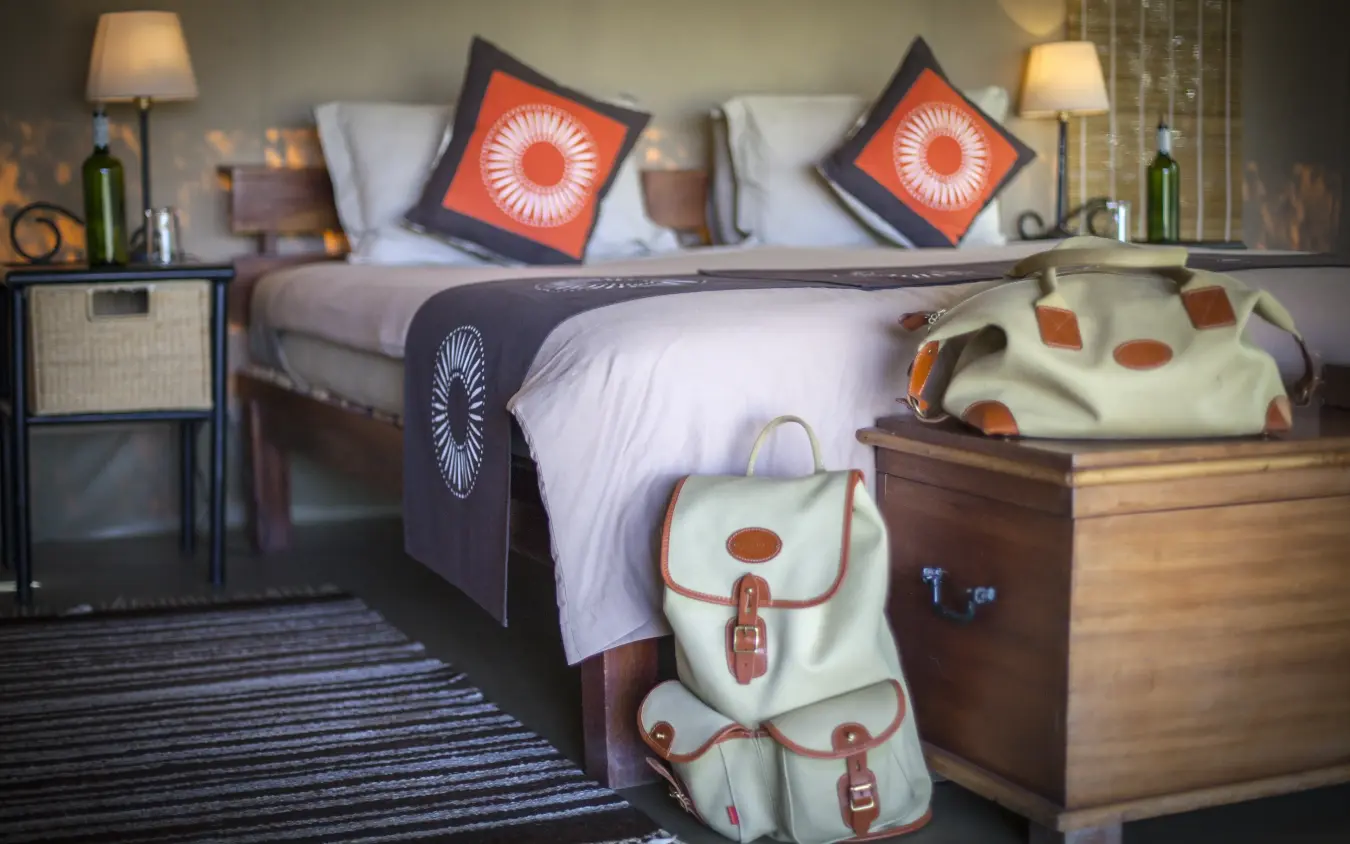 Bedroom with orange accent pillows and cream luggage, Encounter Mara Camp, Maasai Mara, Kenya