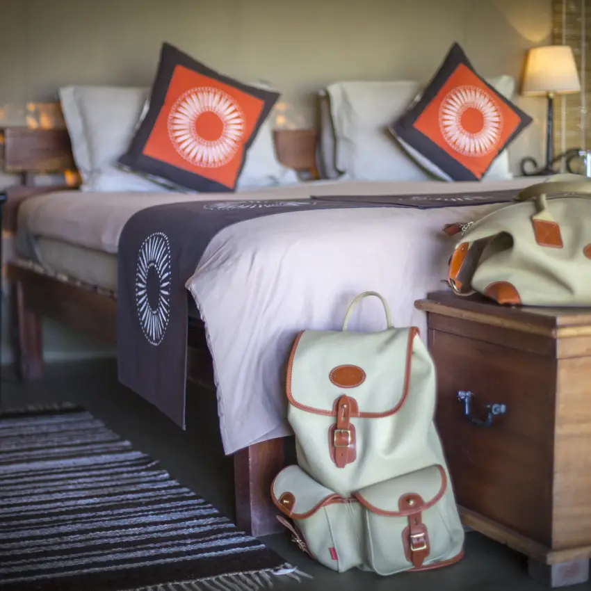 Bedroom with orange accent pillows and cream luggage, Encounter Mara Camp, Maasai Mara, Kenya